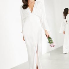 a woman standing in front of a mirror wearing a white dress and holding a bouquet