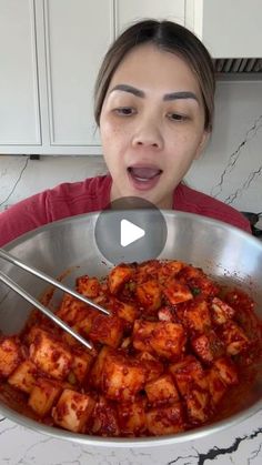 a woman holding a pan full of food with two tongs in it and looking surprised at the camera