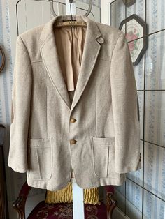 "This jacket is made from wool in timeless beige, in a fine herringbone pattern. It has the original turtle buttons in the front and on the cuffs, two front pockets and two inside pockets, and it's partially lined with tan silky lining. The label reads \"Tailored Especially for The Men's Shop Claremore Okla.\" The measurements, taken with the jacket lying flat, are: shoulder to shoulder, 18 inches; armpit to armpit, 20 inches; sleeves, 25 inches; length, 31 1/2 inches; bottom edge, 25 inches. In very good condition." Beige Tweed Jacket With Lapel Collar For Semi-formal Occasions, Beige Business Blazer With Buttons, Beige Semi-formal Blazer With Buttons, Fall Beige Suits With Buttons, Beige Fall Suits, Cream Single Breasted Sport Coat For Business, Tailored Cream Business Sport Coat, Tailored Cream Sport Coat For Business, Cream Semi-formal Sport Coat With Notch Lapel