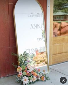 a large mirror sitting on the side of a building next to flowers and greenery