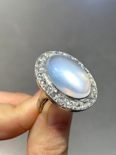 "A dreamy glowing moonstone cabochon ring measuring 2.7 cm by 2.1 cm, encrusted with approximately 1.8 carats of glimmering chunky icy-white rose cut diamonds. The moonstone shines out a eye-catching luminous blue adularescense. Currently measures a size 6. Ring Face Measurement: 2.7 cm by 2.1 cm Measurement of Moonstone: 2.0 by 1.1 cm Approximate Carat Weight of Diamond: 1.8 Carats Gold Purity: 14K Markings: \"14K\" Ring Size: 6.75 (Resizable)" Faceted Moonstone Ring, Luxury Oval Moonstone Anniversary Ring, Heirloom White Moonstone Ring With Rose Cut Diamonds, Luxury White Diamond Moonstone Ring, Luxury White Moonstone Ring With Diamond, Luxury Moonstone Ring With Rose Cut Diamonds, White Moonstone Ring With Rose Cut Diamonds, Formal White Gold Cabochon Moonstone Ring, Luxury Moonstone Gemstone Ring For Anniversary