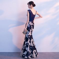 a woman standing in front of a white wall wearing a black and white dress with flowers on it