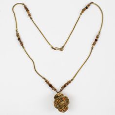 This is part of Chairish’s Costume Jewelry assortment.  French jewelry artist Henry Perichon (aka Henry) designed this elegant brass and Talosel resin necklace in the 1960s. The long necklace features   a brown-beige Talosel resin ball pendant topped with topaz orange crystal faceted rhinestones. The necklace is finished with a gilded brass serpentine chain ornate with natural quartz beads and a hook-closing clasp. This piece is unsigned, but the beige-brown Talosel pendant and the specific orna Vintage Brown Long Necklace As A Gift, Vintage Bronze Beaded Brass Necklaces, Elegant Brown Brass Necklace, Vintage Beaded Necklace With Large Pendant, Vintage Bronze Beaded Chain Jewelry, Vintage Brass Jewelry With Beaded Chain, Vintage Brown Necklace For Formal Occasions, Antique Brown Beaded Necklace, Brown Pendant Necklace In Costume Jewelry Style