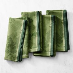 four green napkins are lined up on a white counter top, one is folded and the other has a flower design