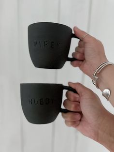 two hands holding black coffee mugs with the words wife and hubby written on them