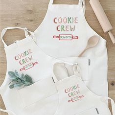 two aprons with cookie crew designs on them next to a wooden spoon and rolling pin