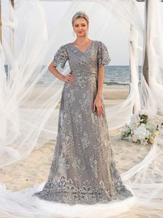 a woman standing on top of a beach next to a white net covered arch with flowers