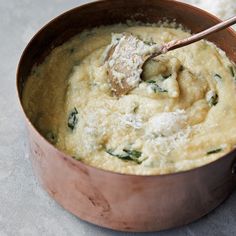 a wooden spoon in a brown pot filled with cheese and spinach dip, ready to be eaten