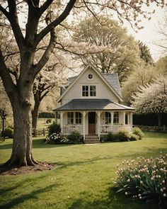 a small white house sitting in the middle of a lush green field next to trees