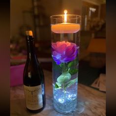 a bottle of wine sitting next to a vase filled with flowers and a lit candle