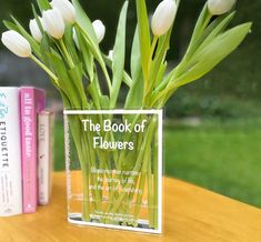 the book of flowers sits next to two books on a table with tulips in it