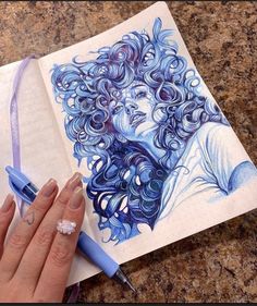 a woman's hand holding a pen and drawing on paper with blue swirls