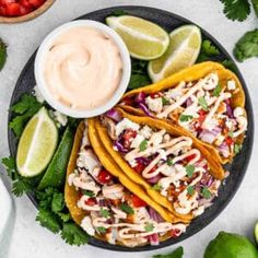 three fish tacos on a plate with limes and strawberries