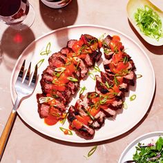 a white plate topped with meat and veggies next to a glass of wine