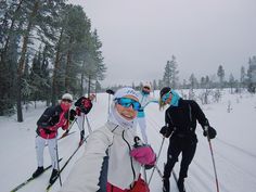 four people on skis in the snow with trees behind them and one person taking a selfie