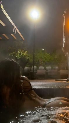 a woman sitting in a hot tub at night with the lights on above her head