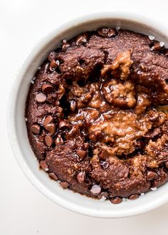 a white bowl filled with chocolate pudding and covered in brownie chunks, on top of a white surface