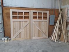 an unfinished garage with two wooden doors and some wood planks on the floor in front of it