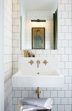 a bathroom sink sitting under a mirror next to a white tiled wall with a painting above it