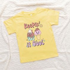 Looking for a cute tee for your kids? We have the perfect Keepin' It Cool Ice Cream graphic tee addition to their closet! Also available in youth tees. Cute Short Sleeve Tops With Cartoon Print, Cute Cartoon Print Short Sleeve Tops, Fun Cotton Top With Cartoon Print, Cute Cotton T-shirt With Cartoon Print, Playful Short Sleeve Cartoon Print Top, Fun Short Sleeve Tops With Cartoon Print, Playful Short Sleeve Top With Cartoon Print, Playful Cartoon Print T-shirt For Spring, Cute Cotton T-shirt With Funny Print