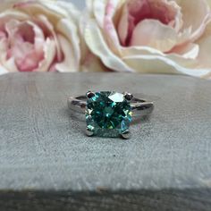 a green ring sitting on top of a wooden table next to pink and white flowers