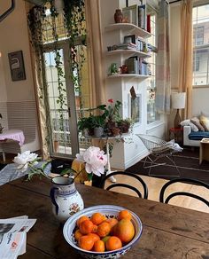 a bowl of oranges sitting on top of a wooden table in front of a window