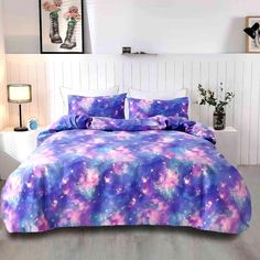 a bed covered in purple and blue comforter with flowers on the pillowcases