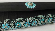 "The perfect wedding purse! A sophisticated and feminine black silk clutch bag, expertly hand embroidered by zardozi artisans. A profusion of petit blue silk flowers are inlaid with emerald gemstones. Each delicate petal and leaf is meticulously outlined with a glittery silver metallic thread, to give a sparkly, opulent 3D effect. Crowned by a beautifully embroidered blue medallion with an emerald cabochon. The word Zardozi means \"gold thread\". It is an elaborate and intricate embroidery art f Elegant Black Hand Embellished Clutch, Elegant Black Hand-embellished Clutch, Traditional Black Clutch With Handwork, Traditional Evening Clutch With Intricate Embroidery, Traditional Black Evening Bag With Handwork, Traditional Clutch Evening Bag With Intricate Embroidery, Black Hand Embellished Clutch For Wedding, Traditional Evening Clutch With Zari Work, Elegant Black Bag With Zari Work