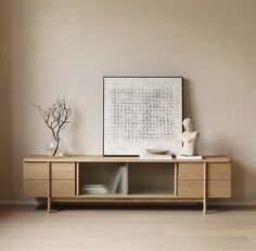 a white vase sitting on top of a wooden table next to a painting and two statues