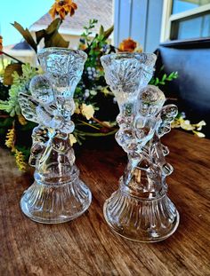 two glass candlesticks sitting on top of a wooden table