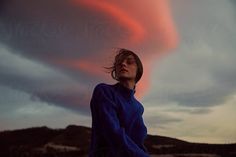 a woman standing in front of a cloudy sky with her head turned to the side