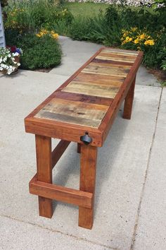 a wooden bench sitting on top of a cement ground next to flowers and trees in the background