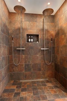 a walk in shower sitting next to a tiled bathroom floor with two hand held shower heads