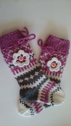 a pair of pink and gray knitted mittens with flowers on the top, sitting on a white surface