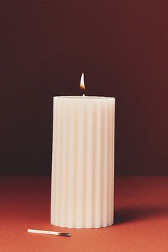 a lit candle sitting on top of a table next to a small matchstick in front of it