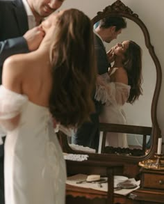 a man and woman standing in front of a mirror looking at their wedding dress on