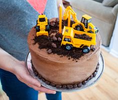 a person holding a cake with construction vehicles on it