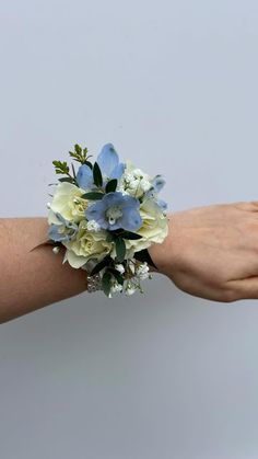 a woman's hand holding a bouquet of white and blue flowers on her arm