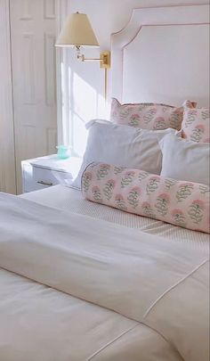 a white bed with pillows and a teddy bear sitting on the pillow in front of it