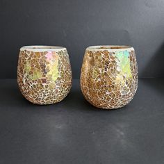 two vases sitting next to each other on a black surface with white and gold designs