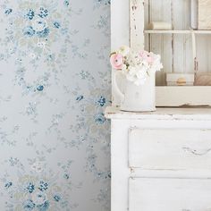 a white vase with flowers sitting on top of a dresser next to a wall paper