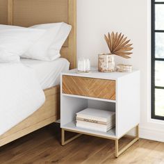 a bedroom with a white bed and wooden nightstand next to a glass vase filled with flowers