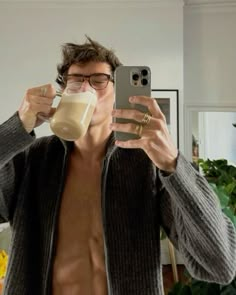 a shirtless man taking a selfie with his cell phone while holding a drink