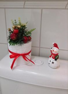 a white toilet with a christmas decoration on top and a snowman figurine next to it