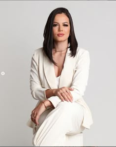 a woman sitting on top of a chair wearing a white suit and heels with her arms crossed