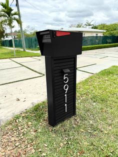 a black mailbox sitting on top of a lush green field next to a sidewalk