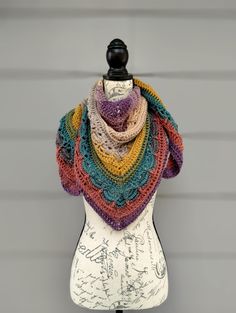 a multicolored crocheted shawl sits on top of a mannequin