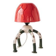 a lamp that is on top of a white base with green legs and red hat