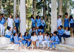 a group of women posing for a photo in front of some columns and trees with blue outfits