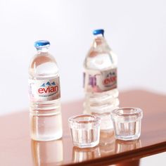 two bottled water bottles sitting on top of a wooden table next to shot glasses and cups